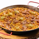 Arroz al horno con trozos de carne y alcachofas, servido en paellera sobre tabla de madera.