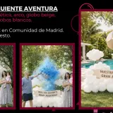 Una familia celebra el **reveal gender** con una explosión de polvo azul. Decoración de globos blancos y un globo aerostático beige crean un ambiente festivo.
