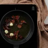 Sartén con aceite, ajos y trozos de pimiento rojo, preparando la base para una salmorreta receta.