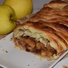 Un delicioso strudel de manzana recién horneado, con su masa dorada y crujiente, relleno de trozos de manzana y pasas.