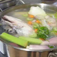 Cabeza de pescado y verduras (zanahoria, apio, cebolla) hirviendo en una olla para hacer un rico caldo de pescado.