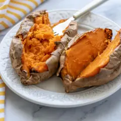 Dos mitades de boniato asado en freidora de aire, servidas en un plato blanco con un tenedor.