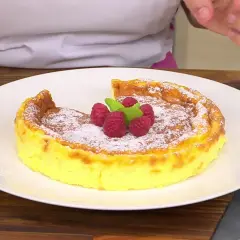 Tarta de queso Eva Arguiñano, dorada y esponjosa, espolvoreada con azúcar glas y decorada con frambuesas y menta.