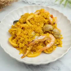 Deliciosa paella de marisco, con gambas, calamares y mejillones, servida en un plato blanco.