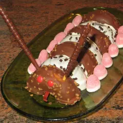 Tarta infantil con forma de oruga hecha de donuts cubiertos de chocolate, decorada con gominolas rosas y barquillos de chocolate.