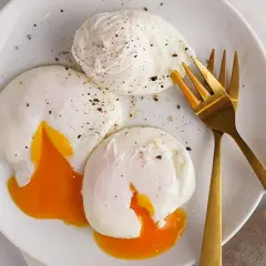 Tres huevos poche perfectamente cocidos, con la yema líquida y dorada, espolvoreados con pimienta negra, listos para disfrutar.