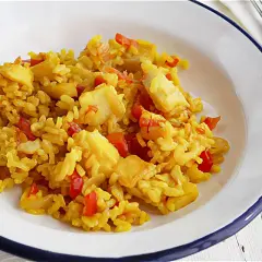 Un plato de arroz con bacalao, pimientos rojos y trozos de pescado blanco. Un delicioso arroz con bacalao listo para disfrutar.