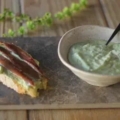 Tosta con mayonesa de aguacate y anchoas. Un cuenco con la cremosa mayonesa de aguacate y una tostada decorada con ella y filetes de anchoa.