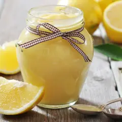 Tarro de lemon curd casero, decorado con un lazo, rodeado de limones frescos y rodajas.