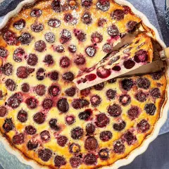 Un delicioso clafoutis de cerezas recién horneado, con una porción servida, espolvoreado con azúcar glas.