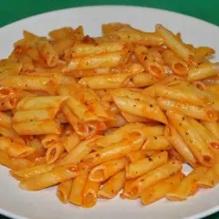 Un plato blanco lleno de macarrones con tomate, cubiertos con una salsa roja y especias.