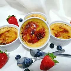 Cuatro cremosos creme brulee con una capa caramelizada, adornados con fresas y arándanos frescos.