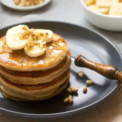 Pila de tortitas esponjosas cubiertas con plátano, nueces y sirope. ¡Una deliciosa receta de tortitas para el desayuno!
