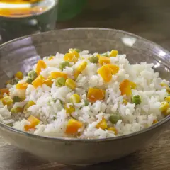 Un tazón de arroz blanco con trozos de zanahoria, guisantes y maíz. Un plato sencillo y colorido de arroz con verduras.