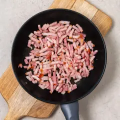 Trozos de bacon crudo en una sartén negra sobre una tabla de madera. Preparando la base para una deliciosa mermelada de bacon.