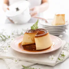 Delicioso flan de queso con caramelo líquido, decorado con una hoja verde y flores delicadas.