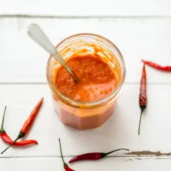 Tarro de cristal con salsa piri piri y chiles rojos alrededor, listo para dar un toque picante a tus platos.