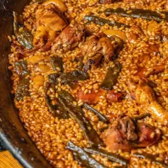 Paella de pollo y judías verdes, con el arroz ligeramente quemado en el fondo, creando un socarrat crujiente.