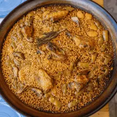 Paella valenciana que lleva pollo, conejo y verduras, con un toque de romero. Un plato tradicional y delicioso.