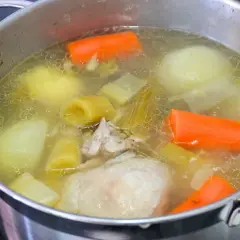 Olla con caldo de pollo casero burbujeante, con trozos de zanahoria, puerro y patata.
