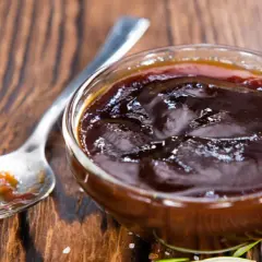 Un cuenco de cristal lleno de deliciosa salsa barbacoa casera, con una cuchara al lado.