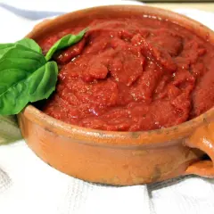 Salsa napolitana casera en cazuela de barro, decorada con hojas de albahaca fresca.