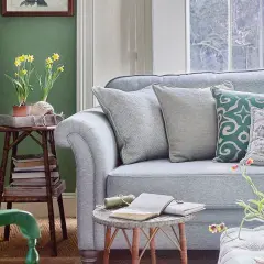 Sofá azul claro con cojines decorativos. Una mesa auxiliar con narcisos y libros complementa la decoración color pastel.