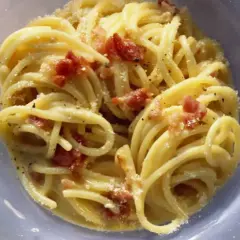 Un plato de pasta carbonara cremoso, con trozos de panceta crujiente y espolvoreado con queso rallado.