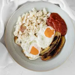 Un plato de arroz a la cubana con dos huevos fritos, plátano maduro frito y salsa de tomate.