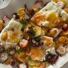 Delicioso plato de pulpo con patatas y huevos rotos, espolvoreado con pimentón y perejil.