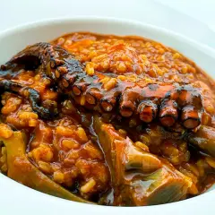 Un tentáculo de pulpo asado reposa sobre un arroz meloso y sabroso, con trozos de alcachofa. Un delicioso arroz con pulpo.