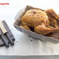 Pollo asado dorado en una fuente, listo para servir. Ideal para tus recetas con pollo. Cubiertos y servilleta a un lado.