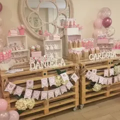 Mesa dulce para comunión de niña, con candy bar casero, globos rosas y blancos, y detalles personalizados.