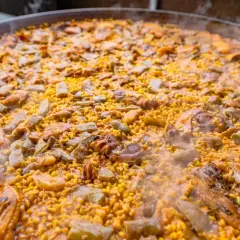 Paella humeante con pollo, judías verdes y trozos de carne. El arroz bomba es el que mejor absorbe el sabor, ideal para esta paella.