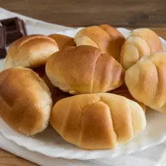 Un plato blanco con pan de leche dorado y suave, junto a trozos de chocolate oscuro.