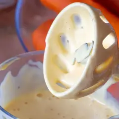 Batidora de inmersión creando mayonesa casera cremosa. Zanahorias al fondo.