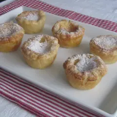 Seis pastelitos de arroz dorados, espolvoreados con azúcar glas, en una bandeja blanca.