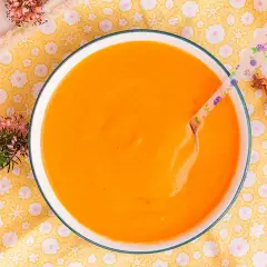 Un tazón de cremosa salsa americana, lista para disfrutar. Una cuchara con flores y una chalota completan la escena.