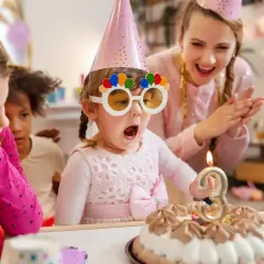 Niños celebran un cumpleaños con pastel y velas. La cumpleañera, con gafas divertidas, sopla la vela. Una temática de cumpleaños para niños llena de alegría.