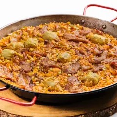 Arroz al horno con trozos de carne y alcachofas, servido en paellera sobre tabla de madera.
