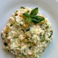 Cremoso arroz a la milanesa con salmón y calabacín, adornado con hojas de albahaca fresca.