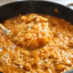 Cuchara sirviendo un delicioso arroz caldoso con pollo y trozos de champiñones.
