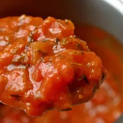 Cuchara llena de sabrosa salsa de tomate casera, con trozos de tomate y hierbas.