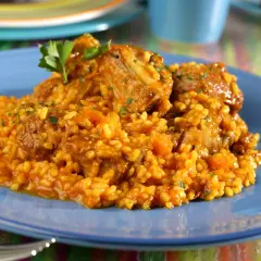 Arroz con costillas, un plato reconfortante con trozos de carne tierna y arroz amarillo, decorado con perejil fresco.