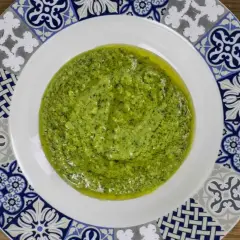 Un plato blanco con un borde decorado con azulejos presenta una generosa porción de vibrante salsa pesto, lista para realzar cualquier plato.