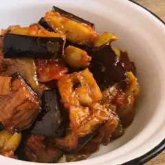 Un plato de caponata siciliana, con berenjenas, aceitunas y tomate, servido en un cuenco blanco.