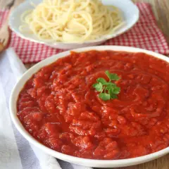 Un tazón de vibrante salsa arrabiata, decorado con perejil, junto a espaguetis y pan.