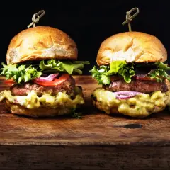 Dos deliciosas hamburguesas caseras con aguacate cremoso, lechuga fresca, tomate y cebolla morada, servidas en panecillos dorados sobre una tabla de madera rústica.