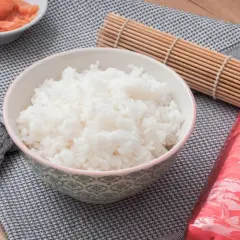 Bol con arroz para sushi, al lado hay salmón, alga nori y un esterilla de bambú.