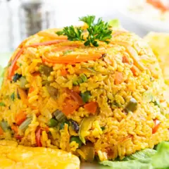 Un montículo de arroz con pollo, adornado con perejil, servido sobre hojas de lechuga y acompañado de plátanos fritos.